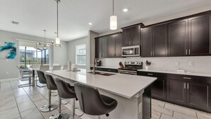 A modern kitchen with dark cabinets, a white island, and bar stools. - Storey Lake Resort, Private Pool, and Much More!! (Kissimmee)