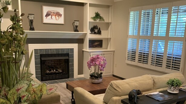 A living room with a fireplace, beige sofa, wooden coffee table, and potted plants.