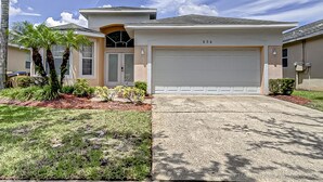 A two-story house with a garage, a driveway, and a well-maintained lawn with palm trees. - Gated Community, Private Pool and Game Room Near Disney!!! (Kissimmee)
