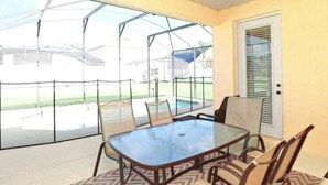 A covered patio with a table and chairs, a ceiling fan, and a view of a swimming pool and houses. - Gated Community, Private Pool and Game Room Near Disney!!! (Kissimmee)