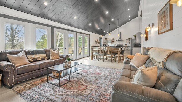 A spacious living area with a large leather sofa, a coffee table, and a patterned rug. There is a dining area with a wooden table and chairs, and a kitchen in the background. - Boyne City- close to golf, lakes, shopping and more!!!  (Boyne City)