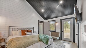 A bedroom with a bed, a chair, a TV, and a door leading to a balcony. - Boyne City- close to golf, lakes, shopping and more!!!  (Boyne City)