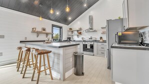 A modern kitchen with a central island, bar stools, a stainless steel trash can, and a built-in oven. - Boyne City- close to golf, lakes, shopping and more!!!  (Boyne City)