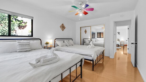 Habitación de hotel con dos camas, ventilador de techo, ventana con persianas y un espejo en la pared.
