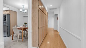Una cocina moderna con armarios de madera, una zona de comedor con mesa y sillas, y un pasillo con suelo de madera.