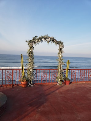 Stunning ocean views surround a beautiful archway adorned with lush foliage and flowers, flanked by two cacti.