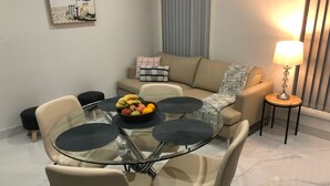 Un salón moderno con una mesa de vidrio rodeada de sillas, un sofá color beige, una mesita auxiliar con una lámpara y un cuadro colgado en la pared.