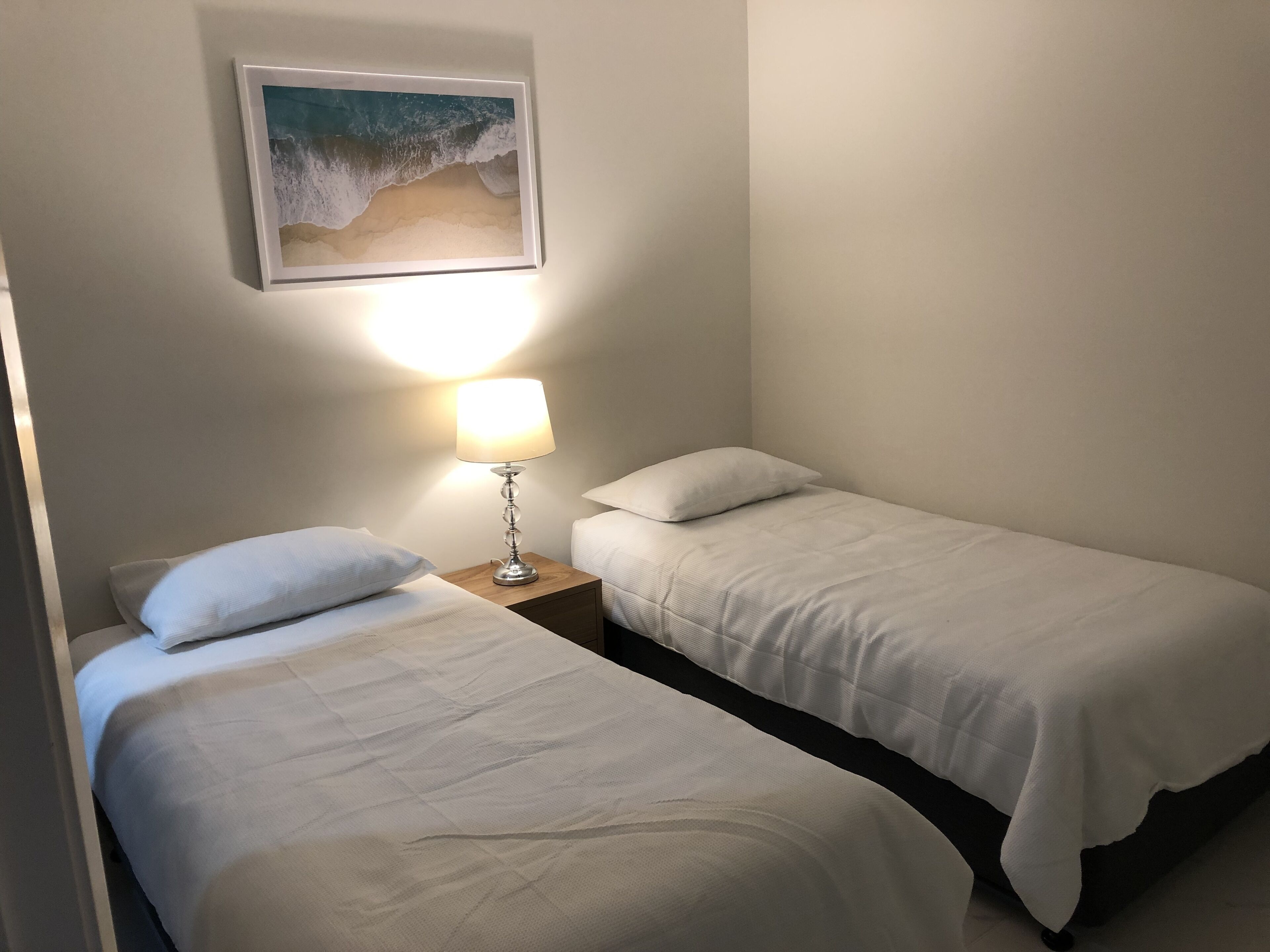 A twin room with two beds, a nightstand with a lamp, and a framed picture on the wall.
