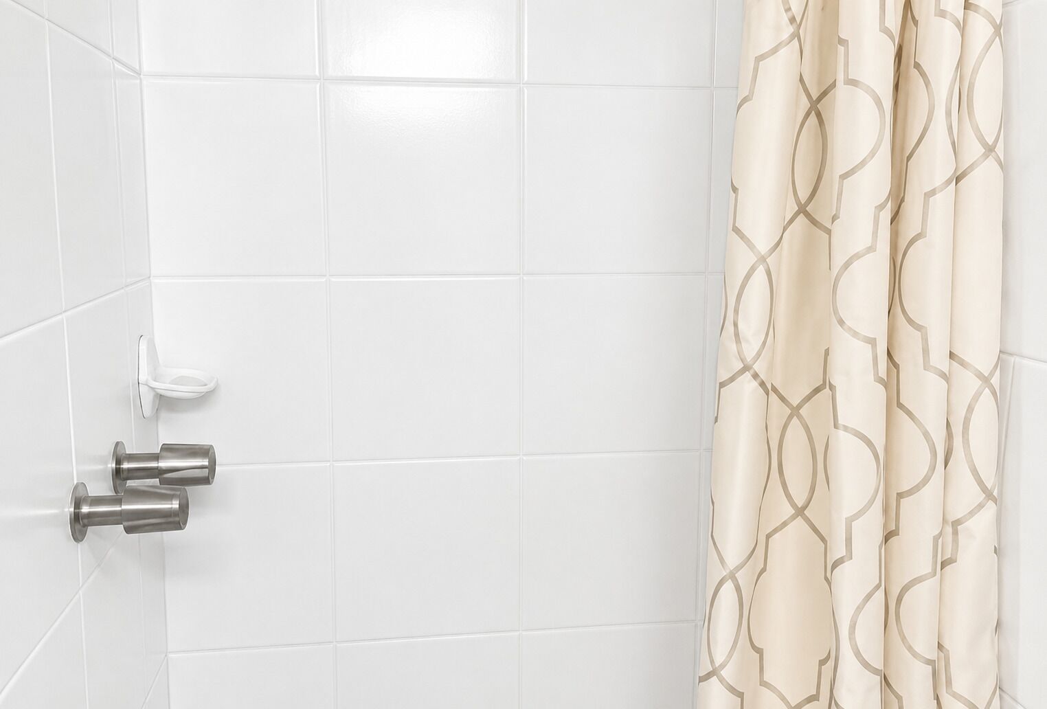 Une salle de bain avec des carreaux blancs, des toilettes dotées d’une poignée de chasse d’eau blanche et un rideau de douche à motifs géométriques.