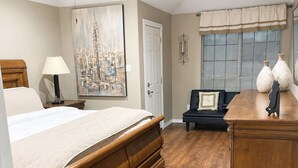 Quarto com cama, escrivaninha, cadeira, ventoinha no teto, quadro e janela com persianas.