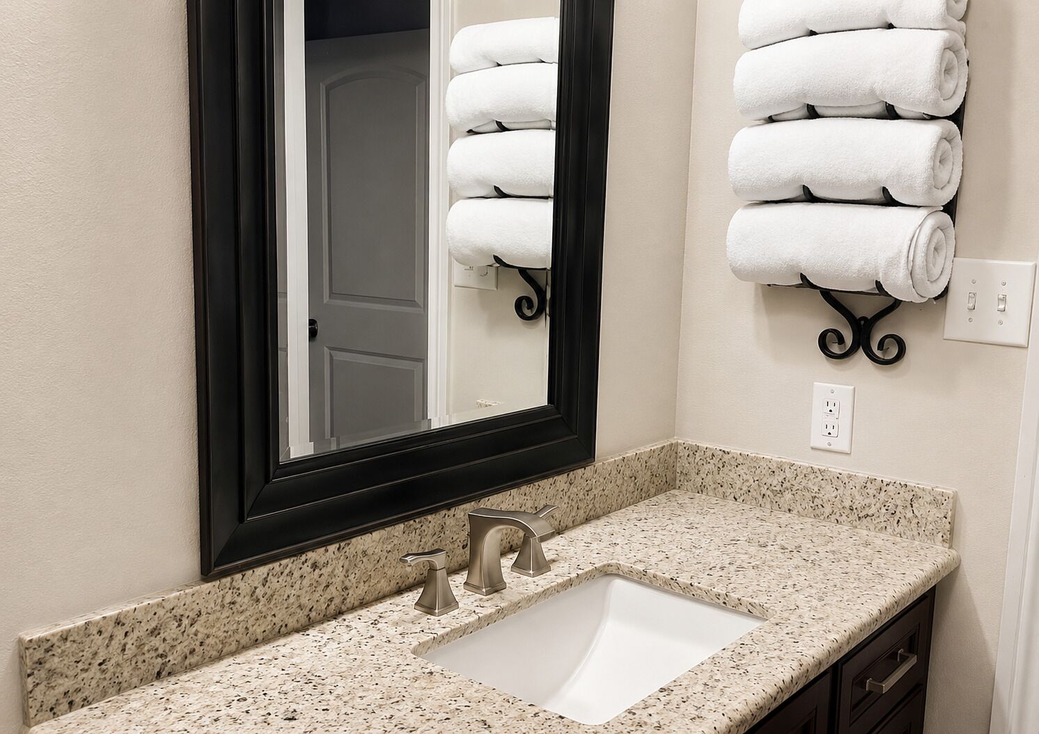 A bathroom with a granite countertop, a sink, a mirror, and a towel rack with folded towels.