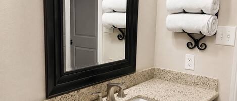 A bathroom with a granite countertop, a sink, a mirror, and a towel rack with folded towels.
