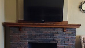 Een woonkamer met een metselwerk open haard, een flatscreen televisie erboven en een vloerbedekking.
