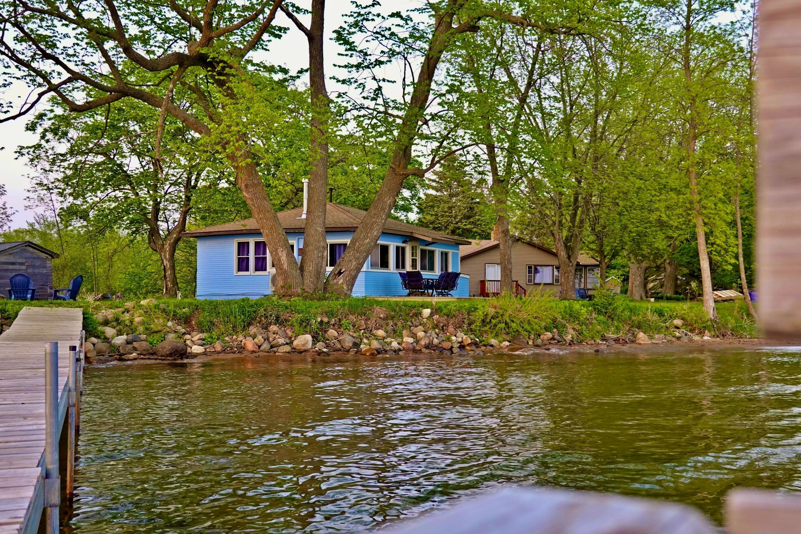 Un chalet au bord du lac, doté d’un quai, entouré d’arbres et bordant une étendue d’eau calme.