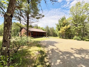 Un chalet rustique doté d’un porche, entouré d’arbres et bordé d’une allée en gravier.