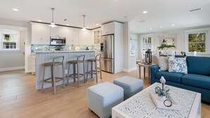 A modern kitchen with white cabinetry, stainless steel appliances, and a bar area with stools. - Back To Blue: Amazing Bean Point Location, Resort Style Backyard with Pool by Anna Maria Life (Anna Maria)