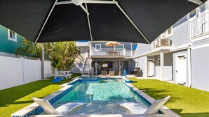 A backyard with a swimming pool, a covered patio, and a two-story house. - Back To Blue: Amazing Bean Point Location, Resort Style Backyard with Pool by Anna Maria Life (Anna Maria)
