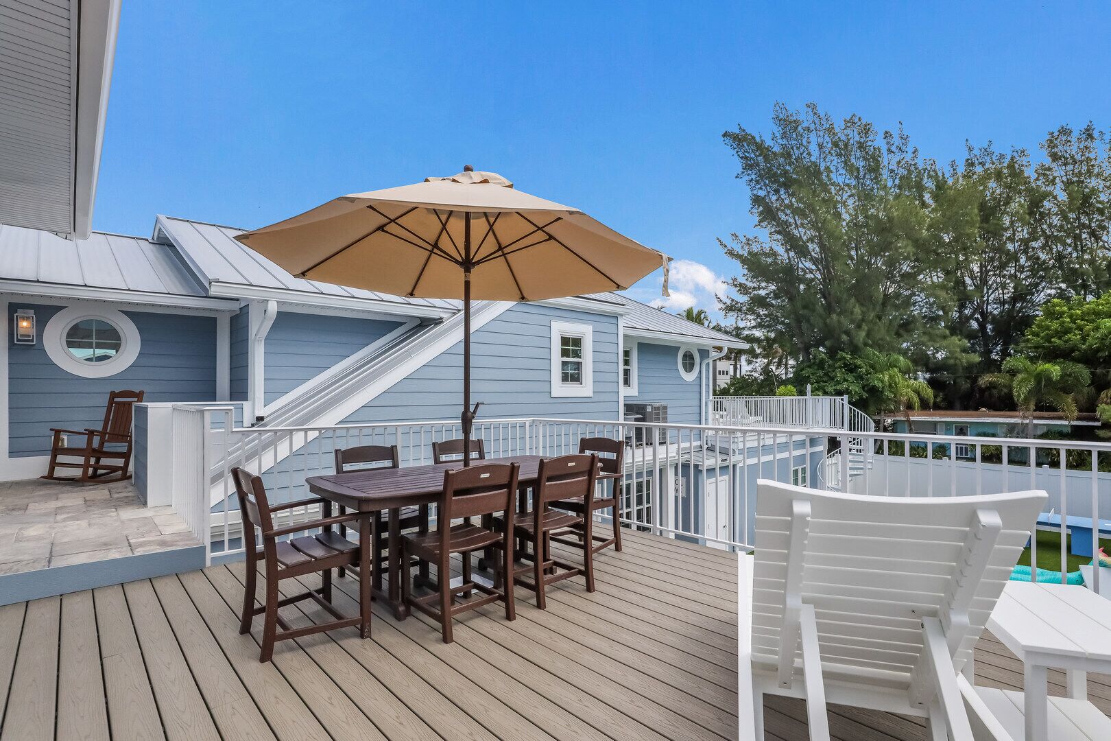 A wooden deck with a table and chairs, a beige umbrella, and a white railing.