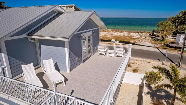 A beachfront property with a covered patio, white outdoor furniture, and a view of the ocean. - Back To Blue: Amazing Bean Point Location, Resort Style Backyard with Pool by Anna Maria Life (Anna Maria)