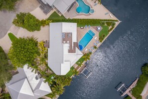 An aerial view of a modern house with a swimming pool, a dock, and a well-maintained lawn.