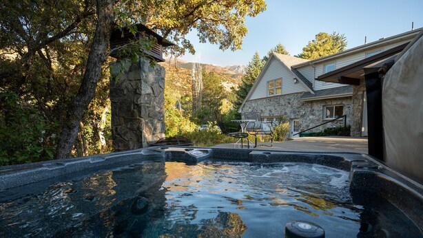 Ein Bereich mit Whirlpool, Steinwänden, einer Steinkonstruktion und Blick auf ein Haus mit Steinverkleidung und überdachter Terrasse.