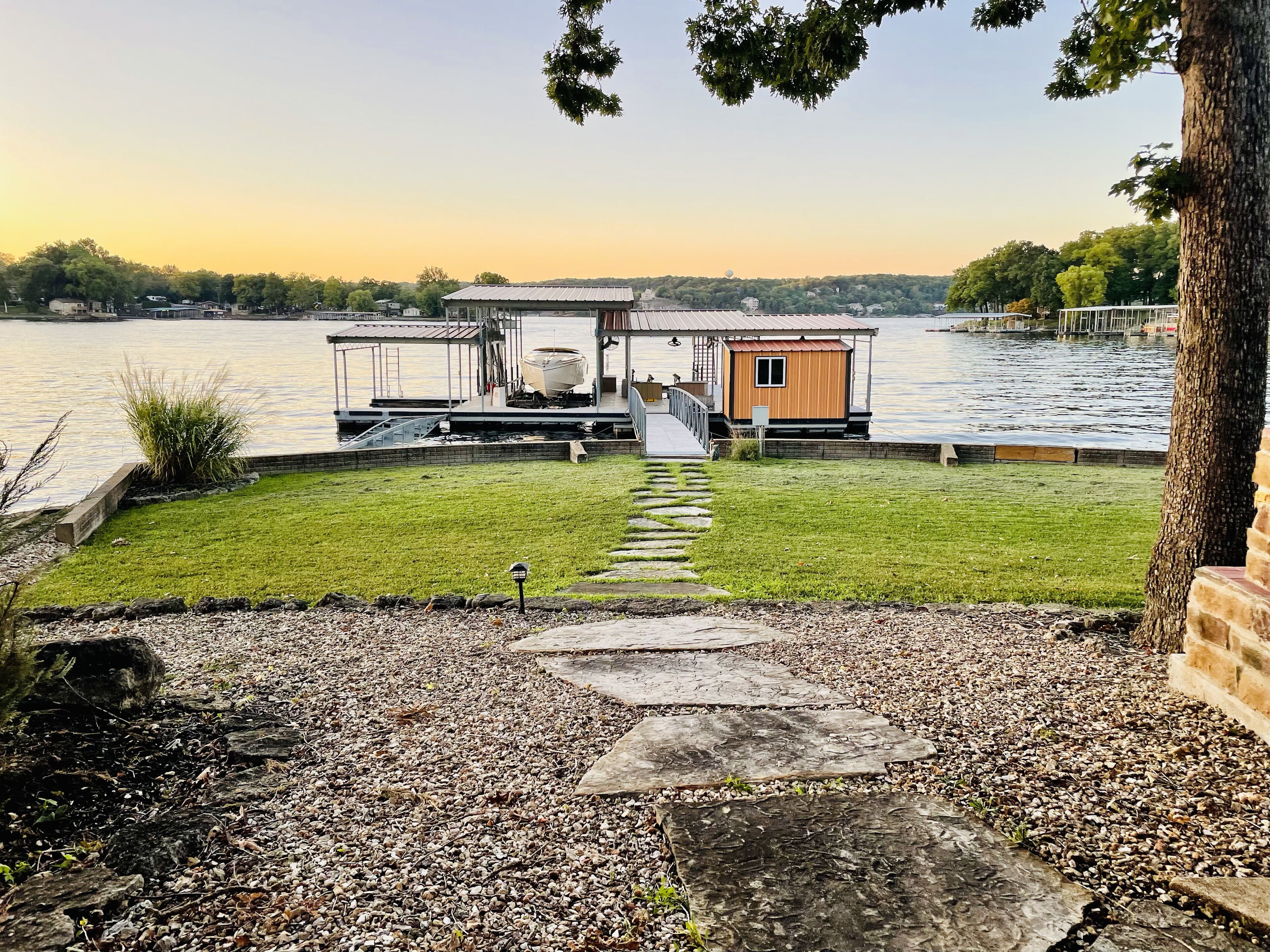 Uma casa à beira do lago com um cais, um gramado e um caminho de pedra que leva ao cais.