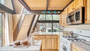 Une cuisine dotée de meubles en bois, d’un four à micro-ondes en acier inoxydable, d’une cuisinière à gaz et d’une grande fenêtre donnant sur un jardin.