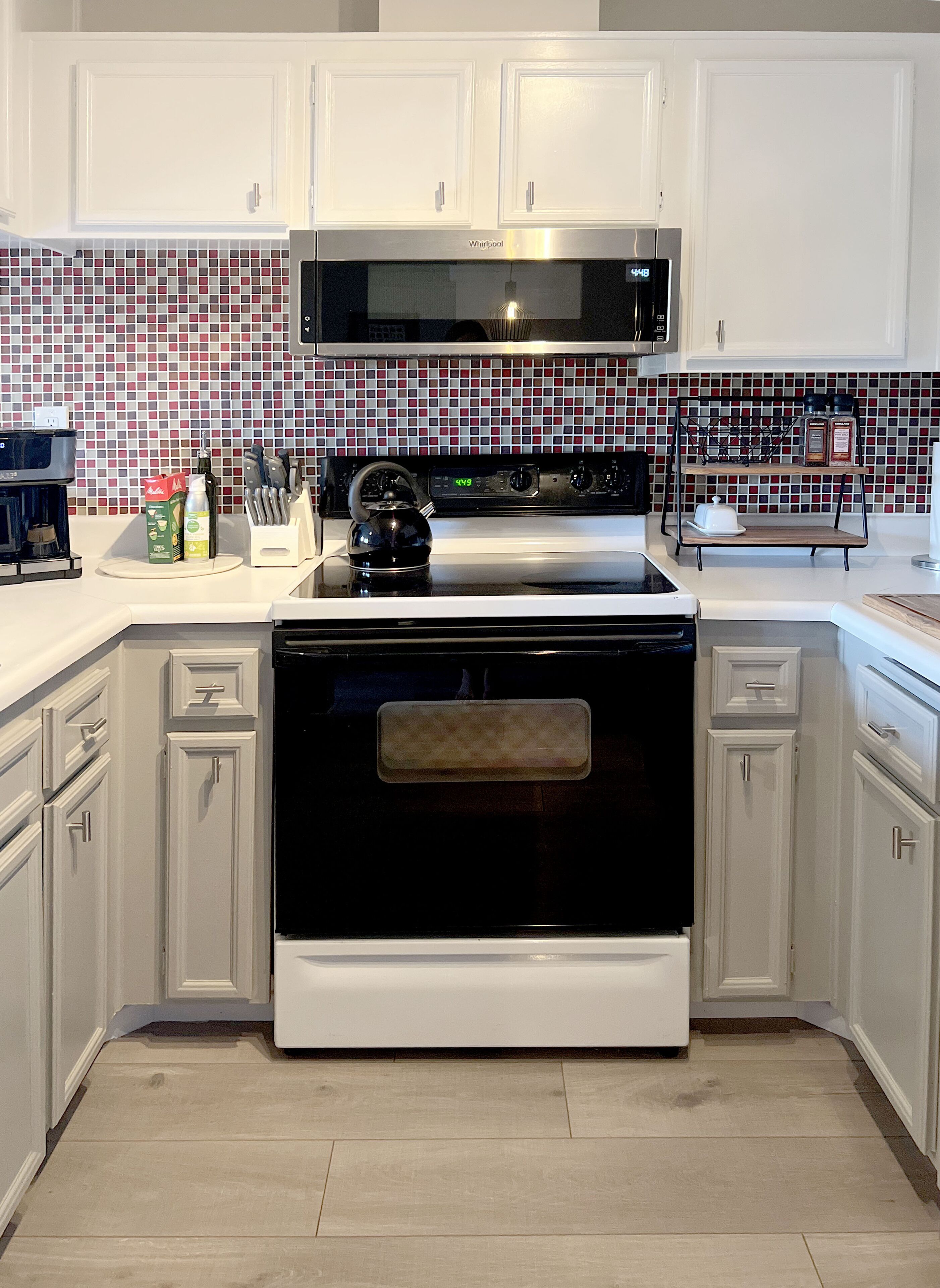 Una cocina con armarios blancos, una estufa negra y un salpicadero de azulejos rojos y blancos.