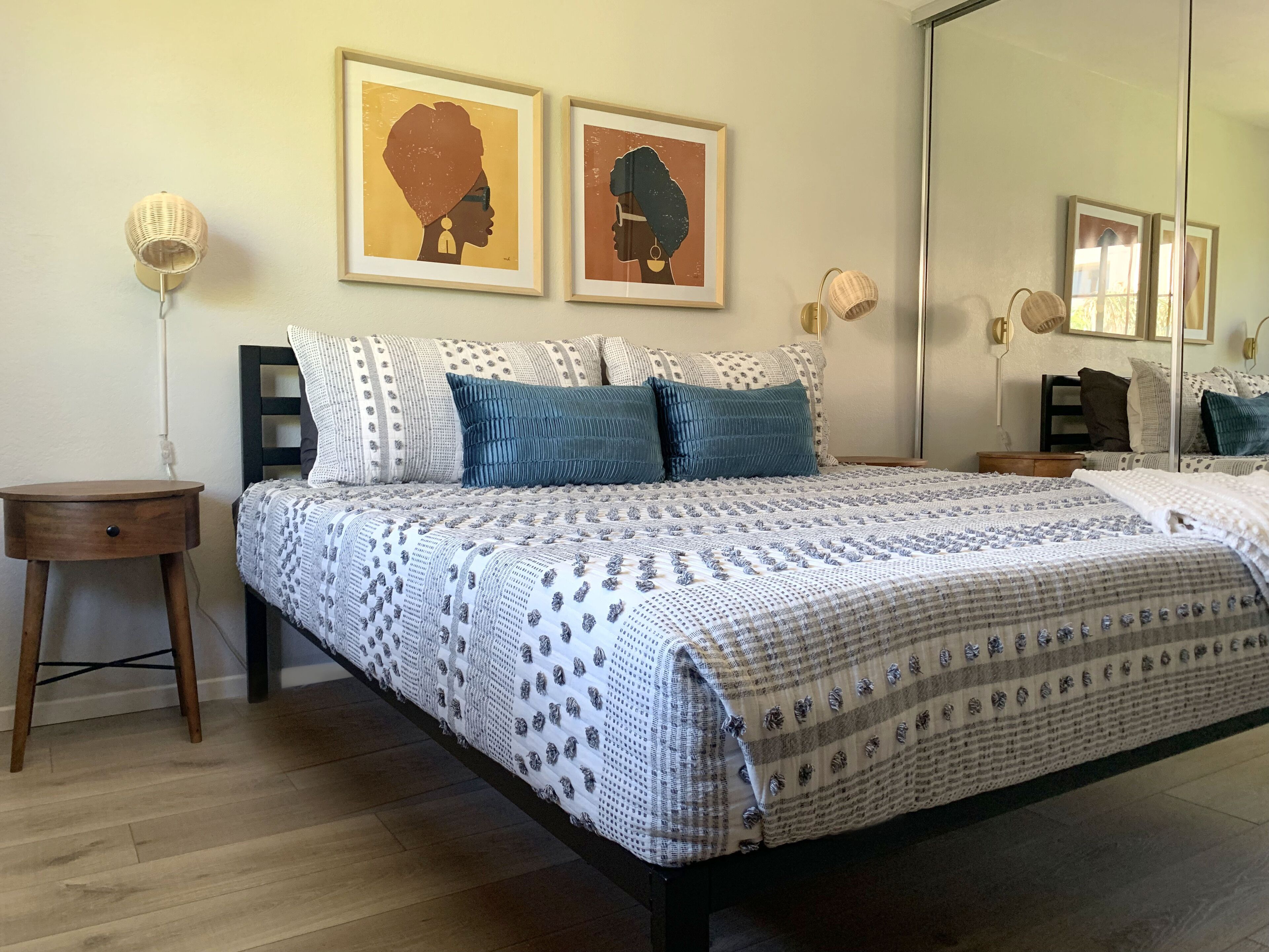 A bedroom with a large bed, two bedside tables, a nightstand, a mirror, and two framed artworks on the wall.