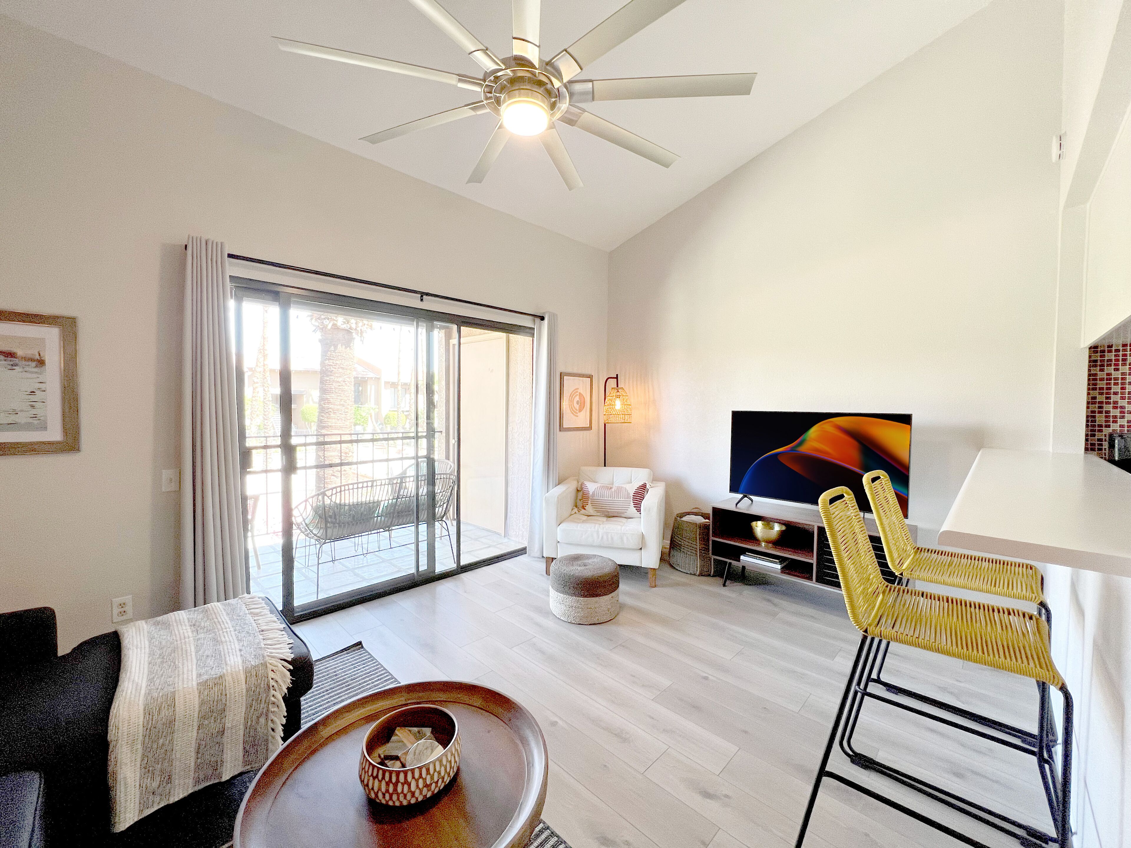 En moderne stue med en ventilator, et fjernsyn, en sofa, et sofabord og et spisebord med stole.