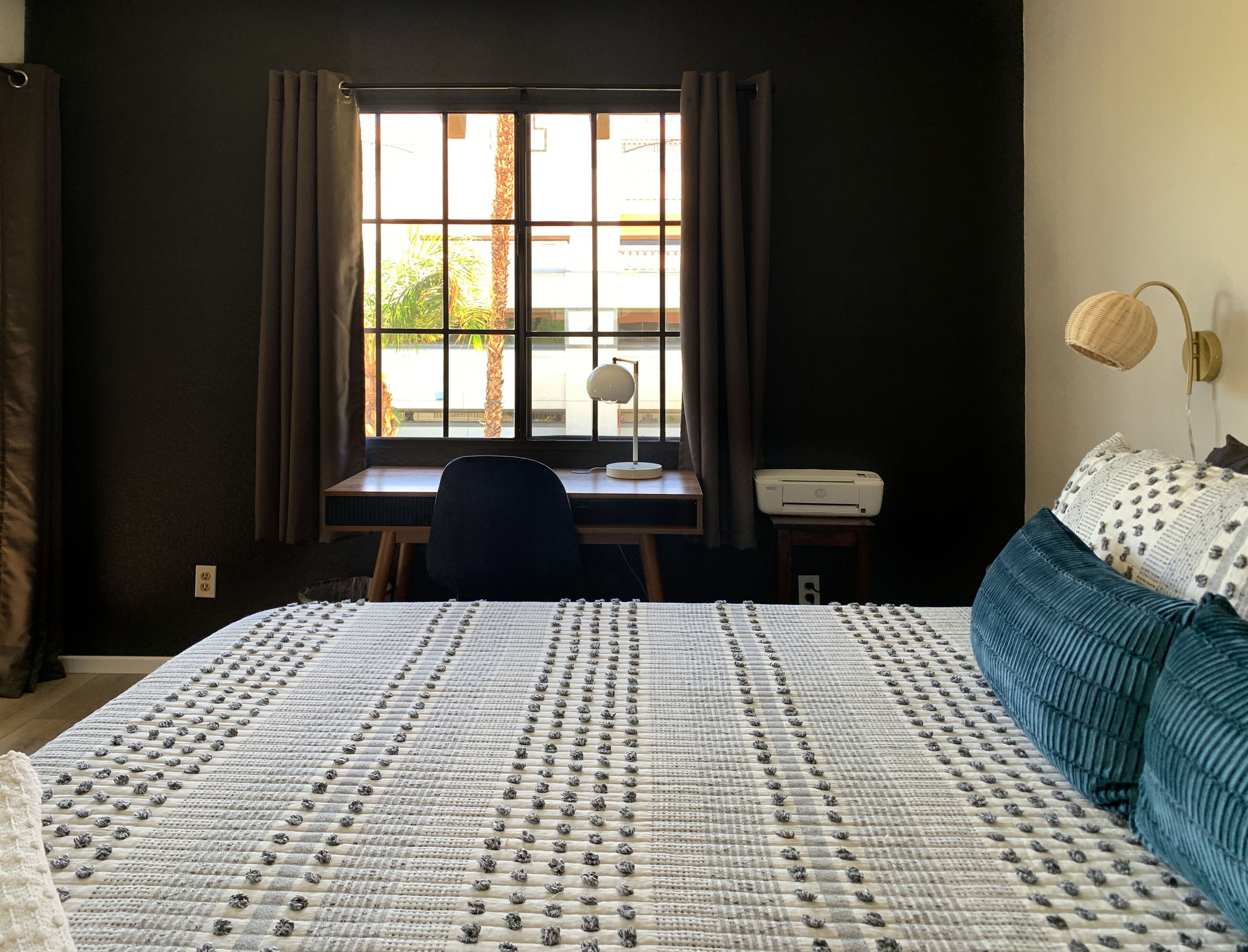 A bedroom with a large bed, a desk with a chair, a printer, and a lamp.
