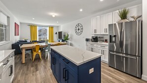 A modern kitchen with a central island, built-in appliances, and a dining area with yellow chairs. - Beach House Steps away from the Boardwalk and Beach with Ocean Views at Seaside… (Seaside Heights)