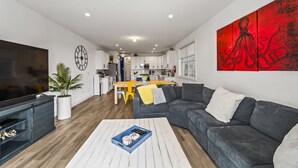 A modern living room with a grey sofa, a coffee table, and a TV. There is a dining area with a yellow table and chairs. - Beach House Steps away from the Boardwalk and Beach with Ocean Views at Seaside… (Seaside Heights)