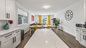 A modern kitchen with white cabinets, a marble countertop, and a dining area with a wooden table and yellow chairs. - Beach House Steps away from the Boardwalk and Beach with Ocean Views at Seaside… (Seaside Heights)