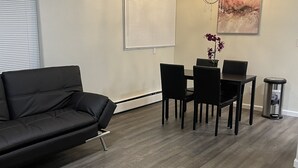 Un salon moderne avec un canapé en cuir noir, une table à manger avec des chaises, une machine à café et une œuvre d’art accrochée au mur.