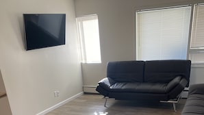 Ein Wohnzimmer mit flachbildfernseher an der Wand, einem schwarzen Ledersofa und Holzboden.