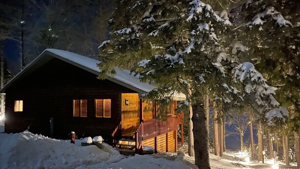 Una cabaña con fachada de madera, un porche y un paisaje cubierto de nieve.