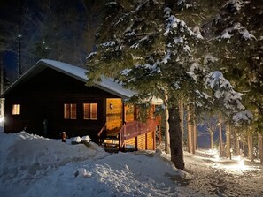 A cabin with a wooden exterior, a porch, and a snow-covered landscape.