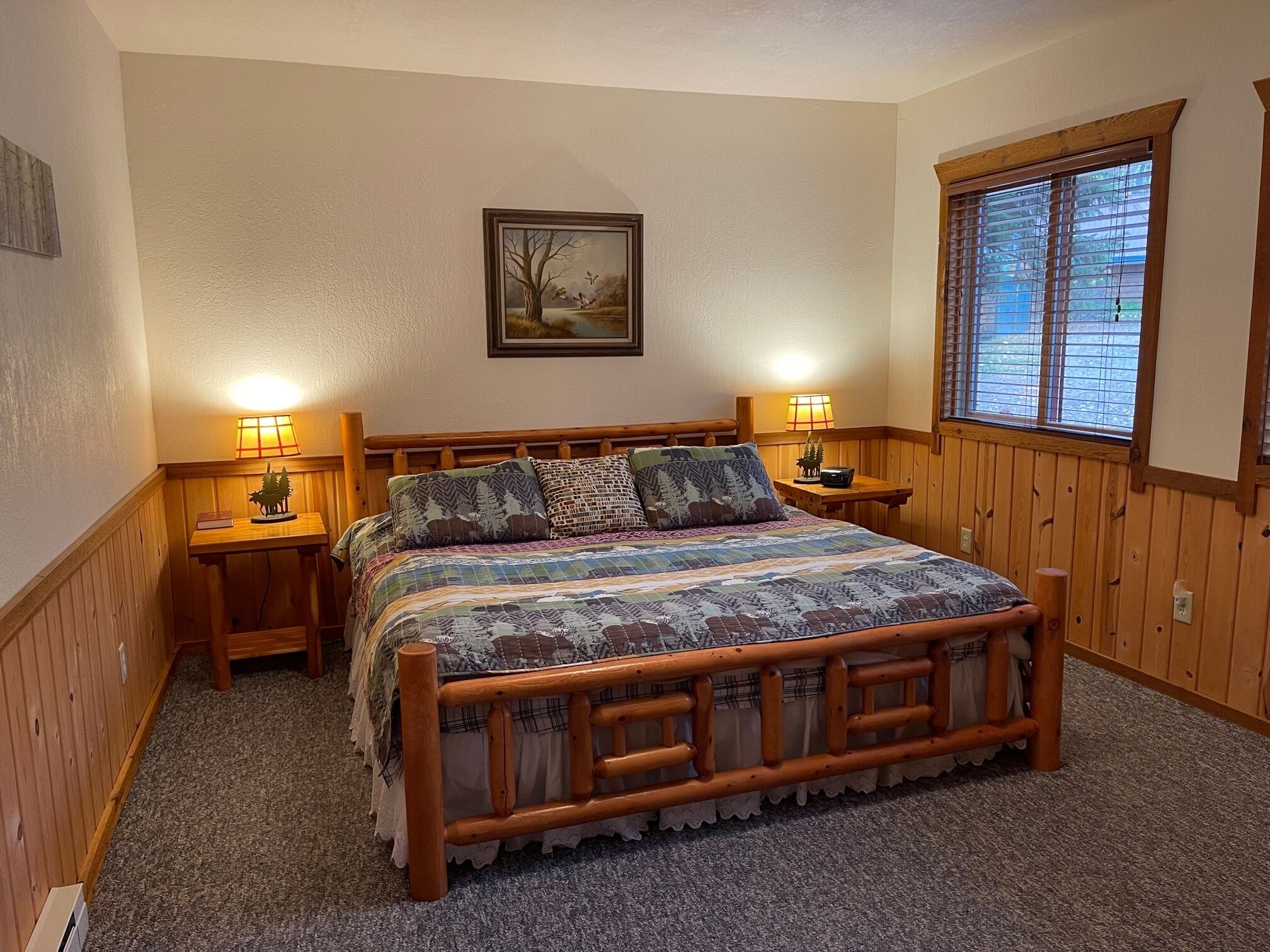 Une chambre confortable avec un lit en bois, deux tables de chevet avec des lampes, un tableau encadré au mur et une fenêtre avec des stores.
