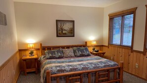 Un dormitorio acogedor con una cama de madera, dos mesitas de noche con lámparas, un cuadro enmarcado en la pared y una ventana con persianas.