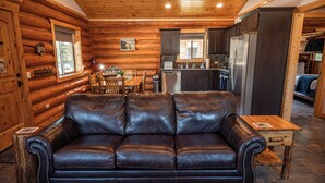 A log cabin interior with a leather sofa, wooden dining table, and kitchen area.