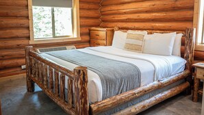 A wooden log cabin room with a large bed, a window, and a wooden nightstand.