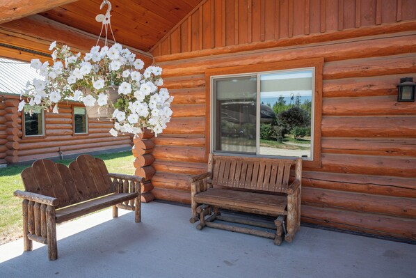 A wooden cabin with a bench and hanging flowers.