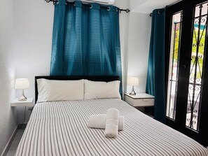 A hotel room with a bed, two bedside lamps, a window with curtains, and a view of greenery outside.
