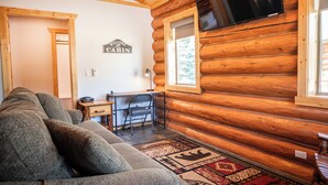 A log cabin interior with a sofa, a desk, and a television mounted on the wall.