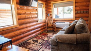A log cabin interior with a sofa, a wooden chair, a table, and a patterned rug.
