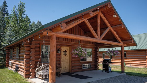 A log cabin with a porch, a grill, and hanging flower baskets.