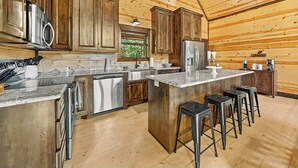 A kitchen with wooden cabinets, stainless steel appliances, and a bar area with stools. - 3 King Suites, Hot Tub, Firepit, Playset, Dogs OK (Broken Bow)