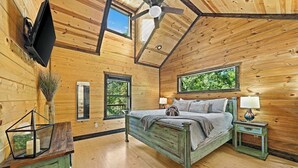A wooden cabin bedroom with a bed, bedside tables, a ceiling fan, and windows. - 3 King Suites, Hot Tub, Firepit, Playset, Dogs OK (Broken Bow)