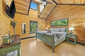 A wooden cabin bedroom with a bed, bedside tables, a ceiling fan, and windows. - 3 King Suites, Hot Tub, Firepit, Playset, Dogs OK (Broken Bow)